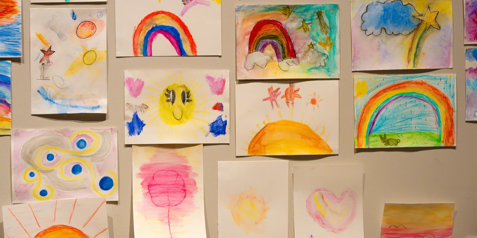 Children's paintings of rainbows, suns and hearts pinned up on a wall