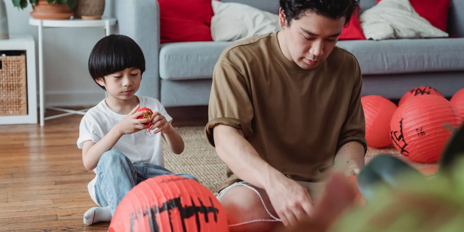 A boy and a man sit on a living room floor among red paper lanterns