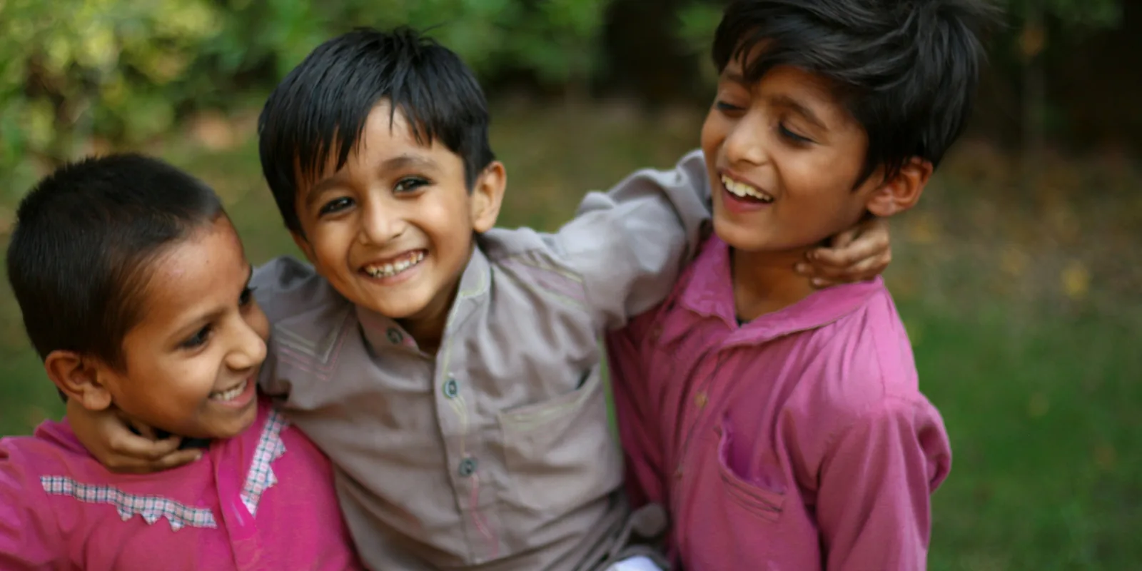Three laughing boys in kurtas with their arms round each other in a garden