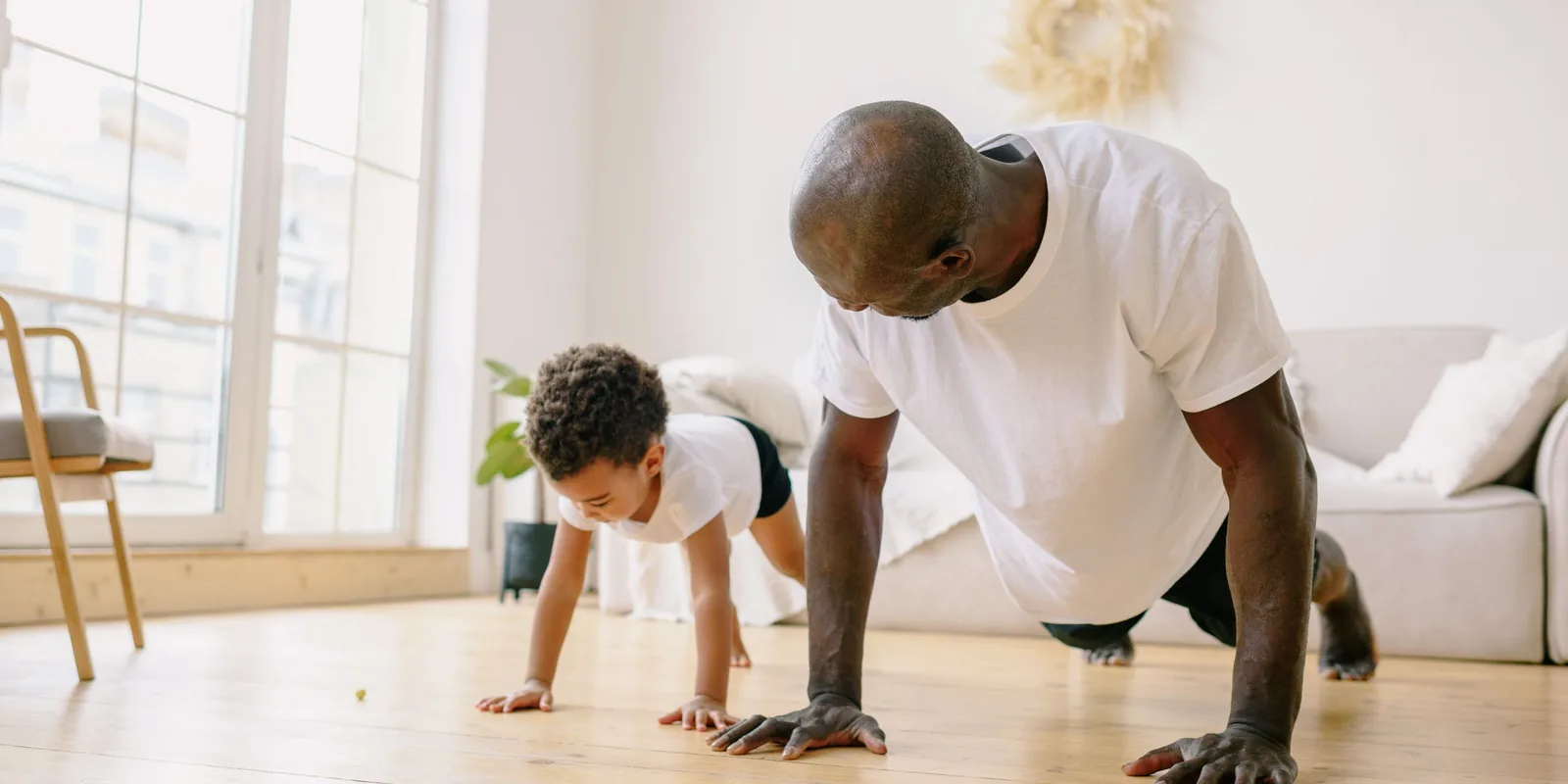 A man and a small boy do press-ups side by side on a living room floor