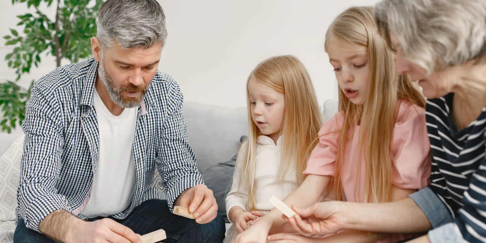 A man, two young girls and a grey-haired woman play a wooden block-stacking game together on a sofa