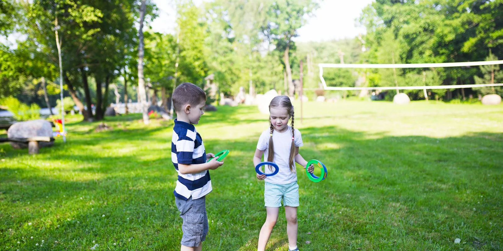 A boy and a girl play ring toss on a sunny lawn