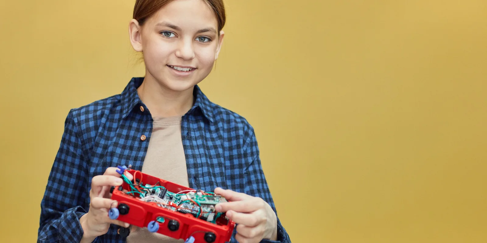 A smiling girl holds a red robot kit she has built