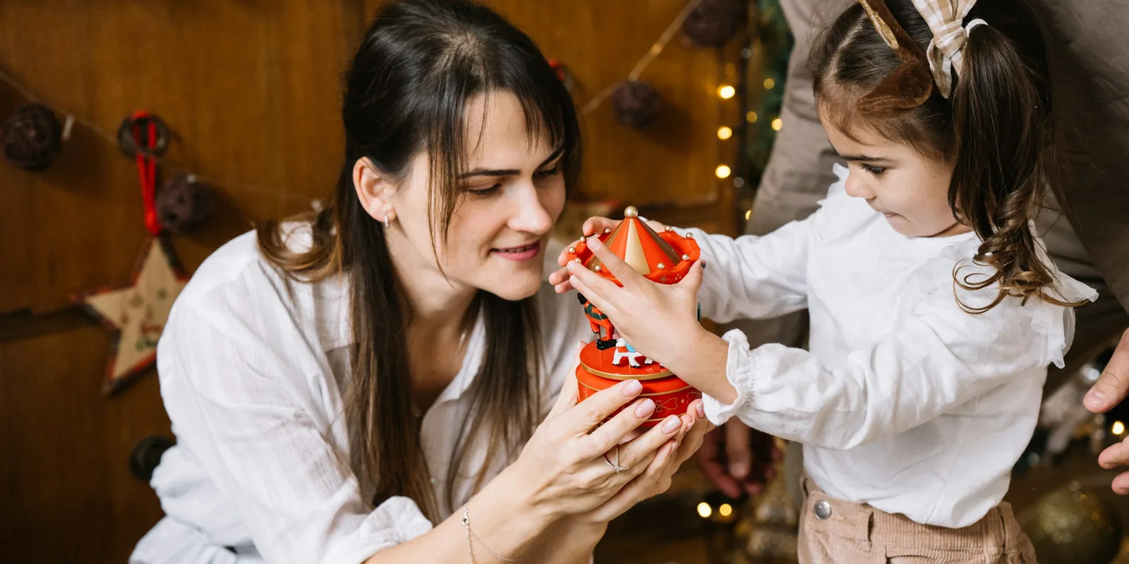 A woman and a little girl hold a red musical carousel together in a room decorated for Christmas