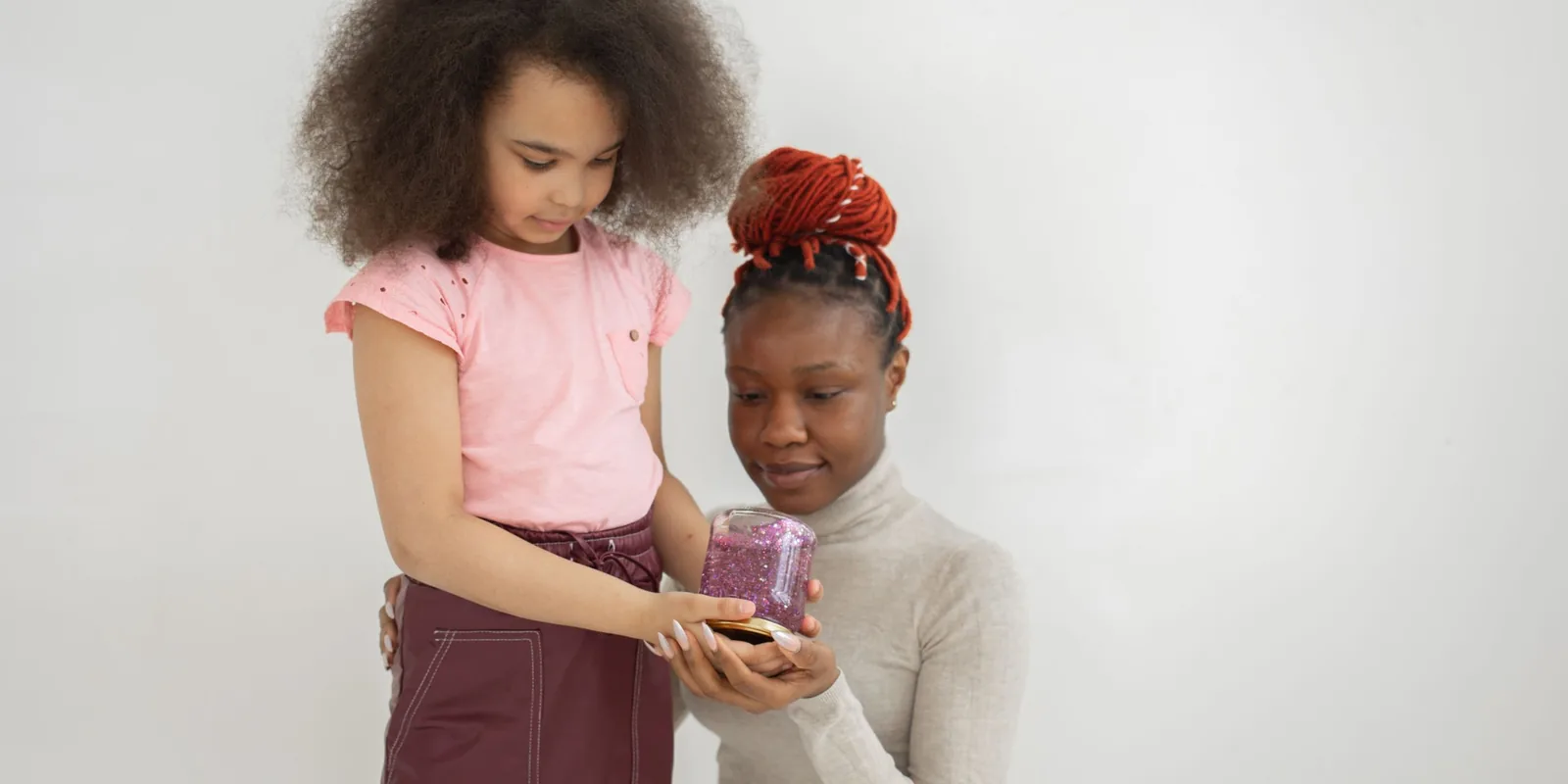 A girl shows a woman a small jar filled with purple glitter