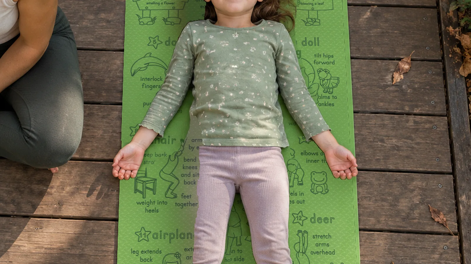 A child lying flat along a green Yogi-Me mat on garden decking, seen from above