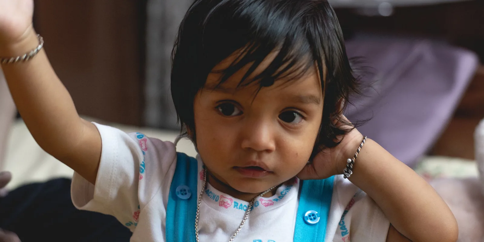 A young girl with dark hair rests one hand behind her ear and raises her other arm