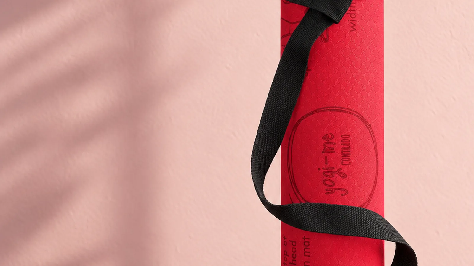 A rolled red Yogi-Me mat standing upright against a pink wall