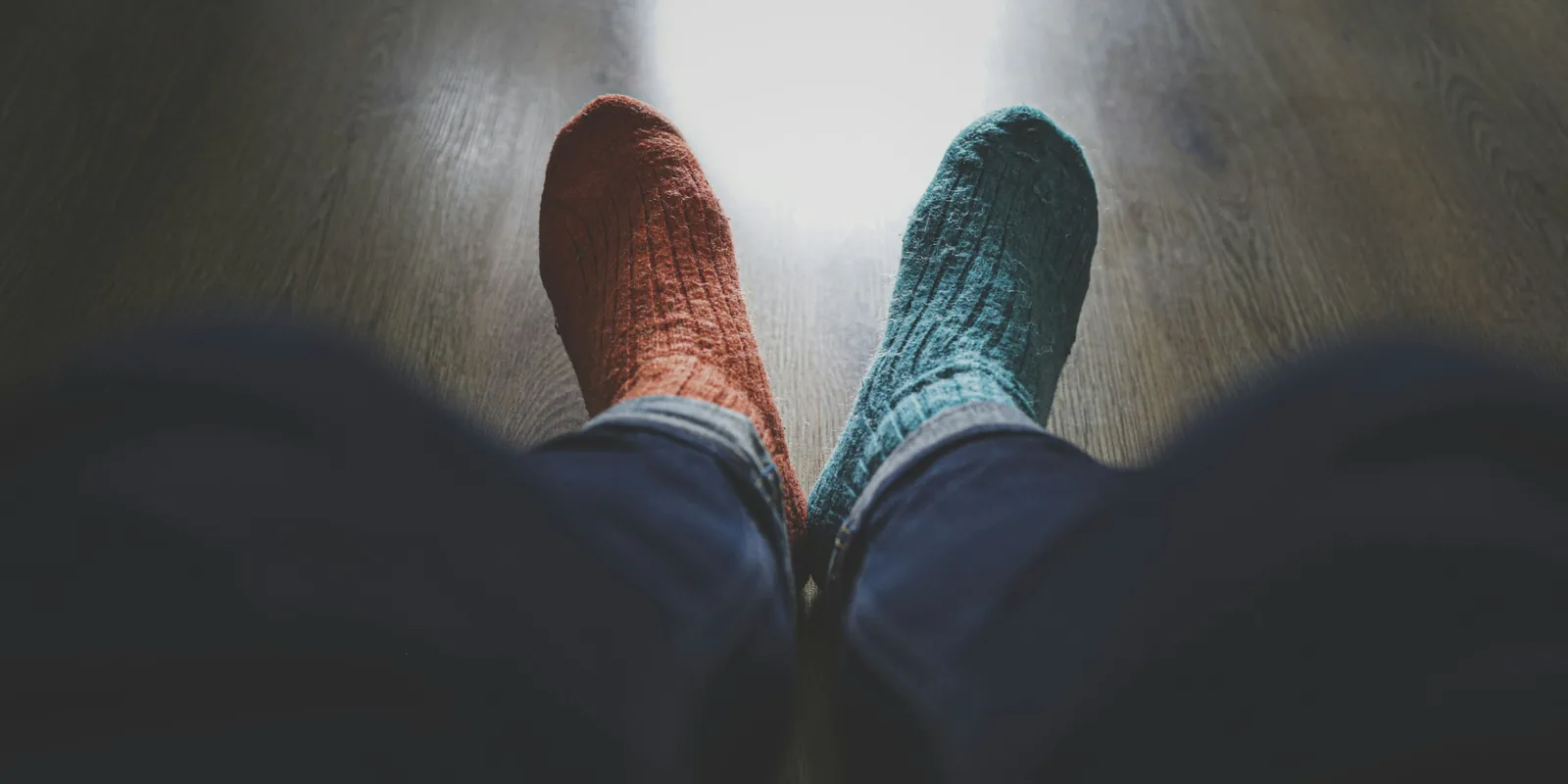 Feet in one orange sock and one green sock rest on a wooden floor