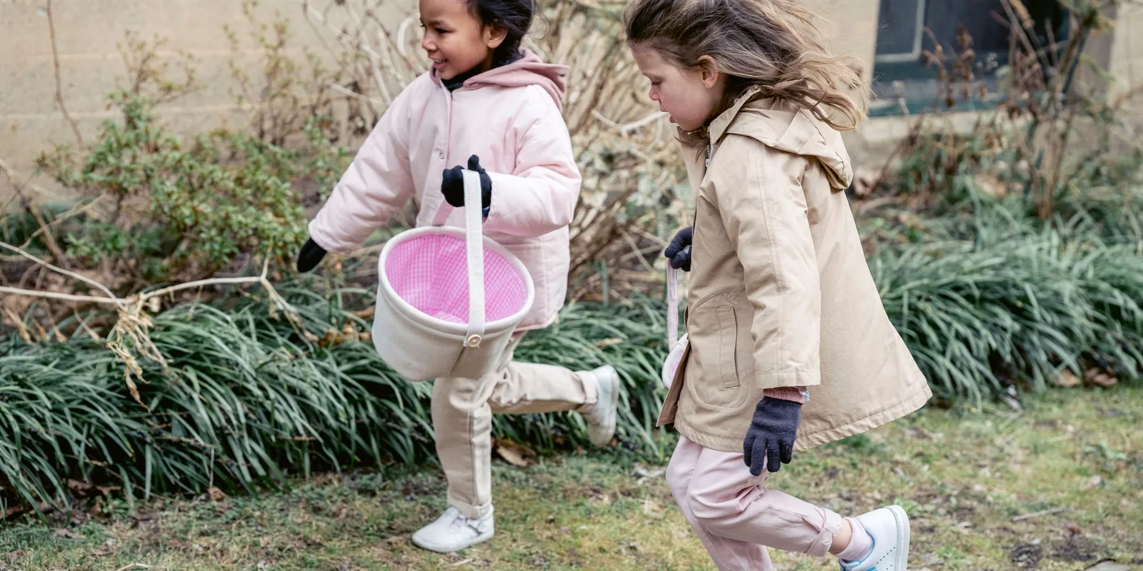 Two girls in winter coats run across a garden carrying small baskets