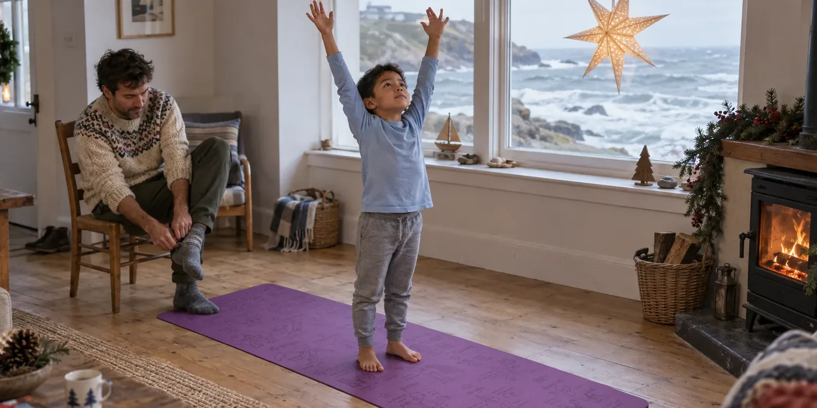 A boy reaches both arms high on a purple Yogi-Me mat in a seaside living room while an adult sits nearby