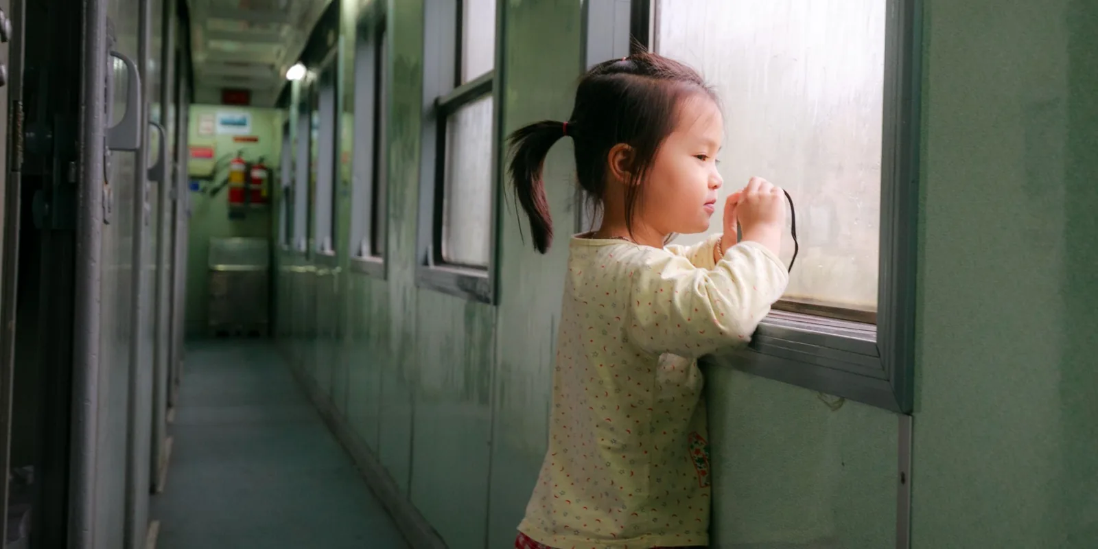 A young girl stands in a train corridor and looks out of the window