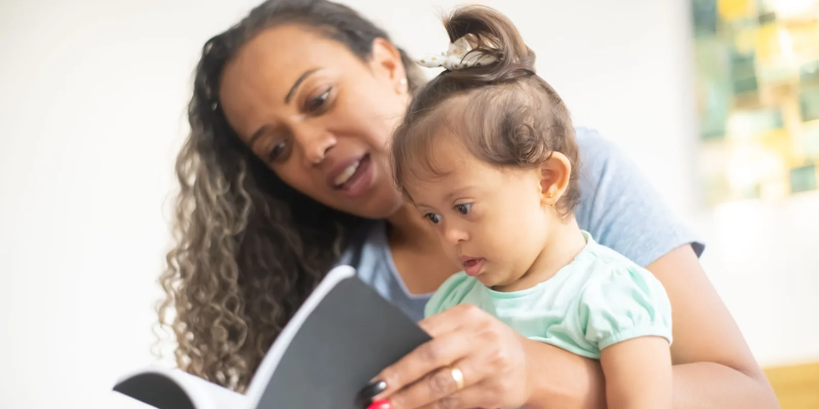 A woman reads aloud from a small book to a toddler sitting on her lap