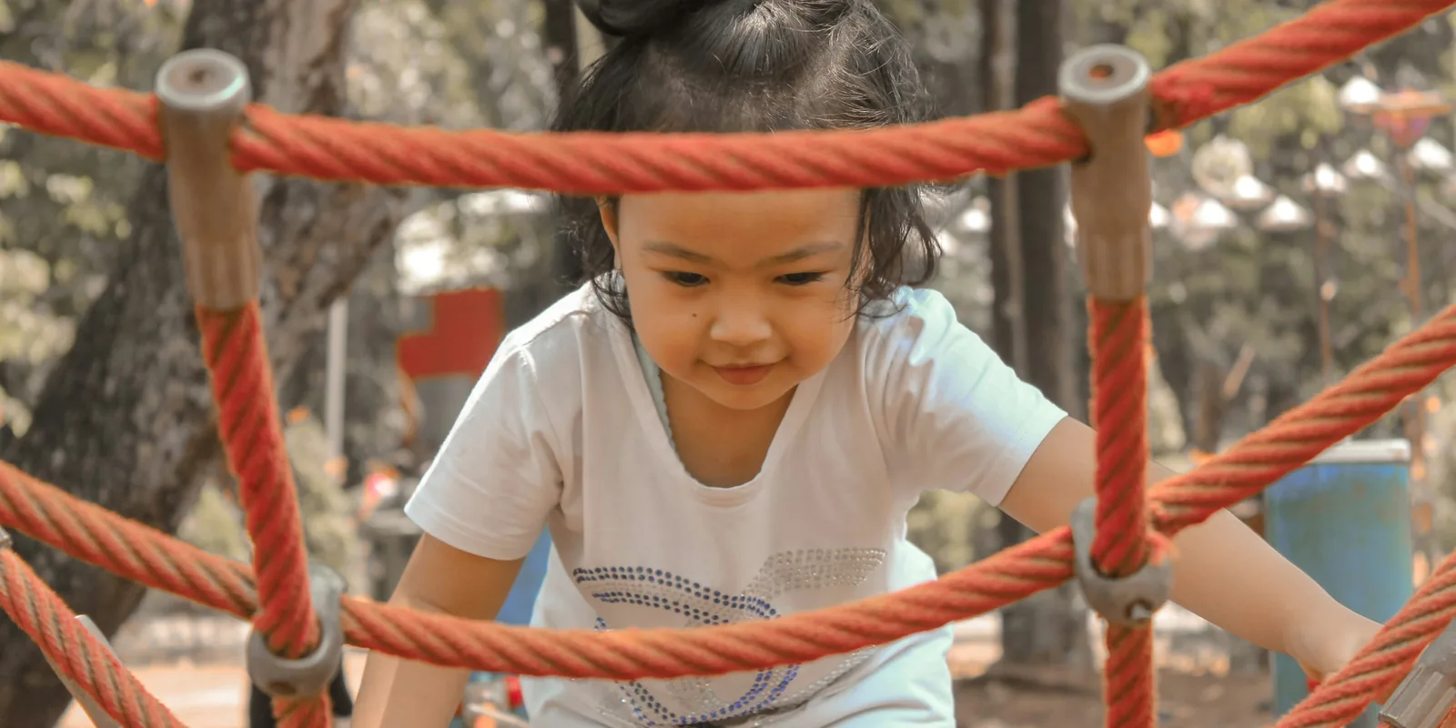 A young girl climbs through an orange rope net in a playground