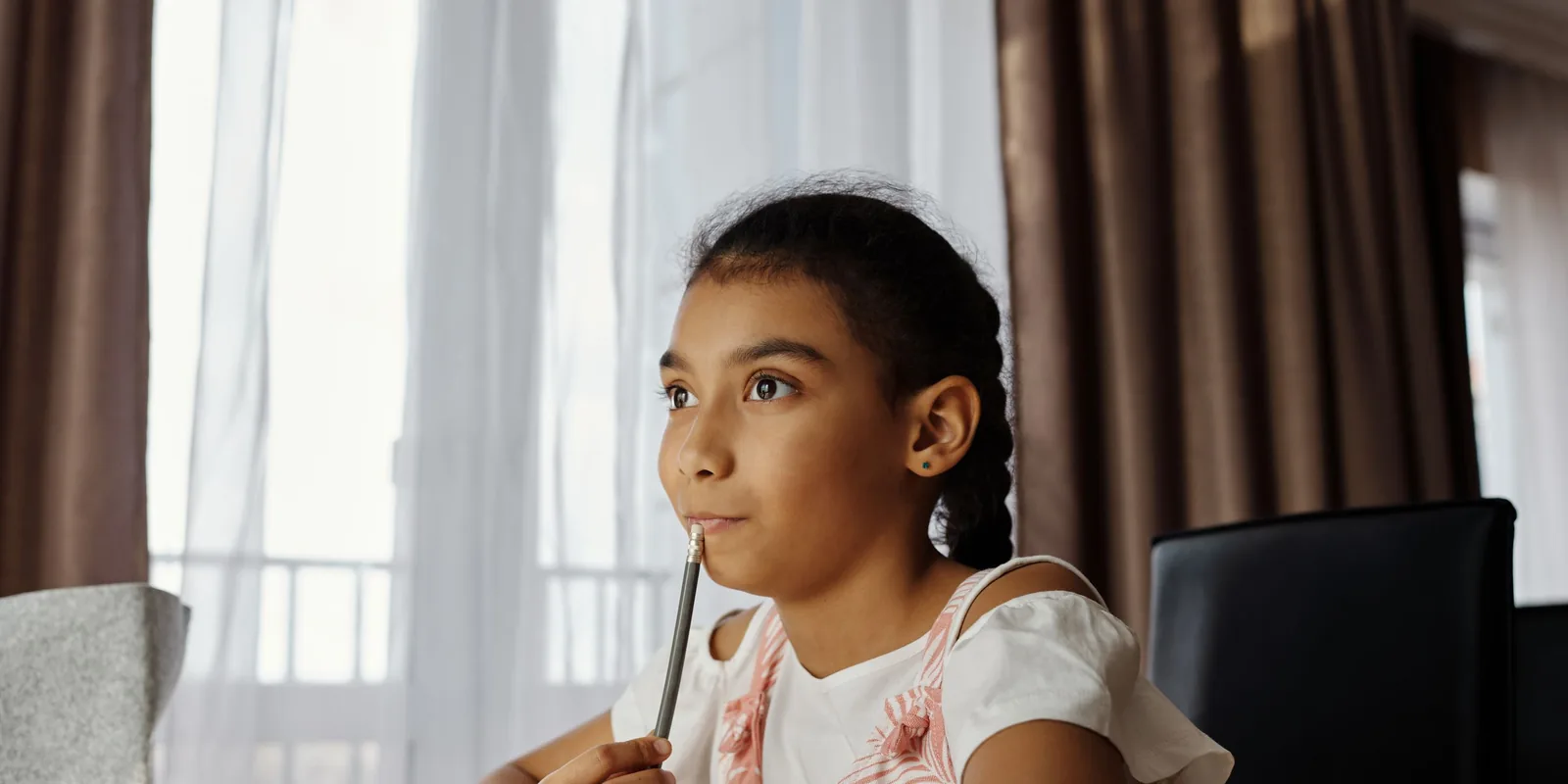 A girl rests a pencil on her lip and looks up while she thinks