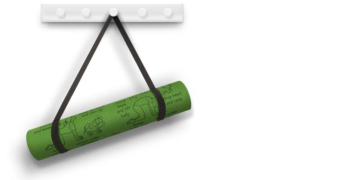 Green Sun Salutation kids' yoga mat rolled up and hanging by its carry strap from a white wall peg rail